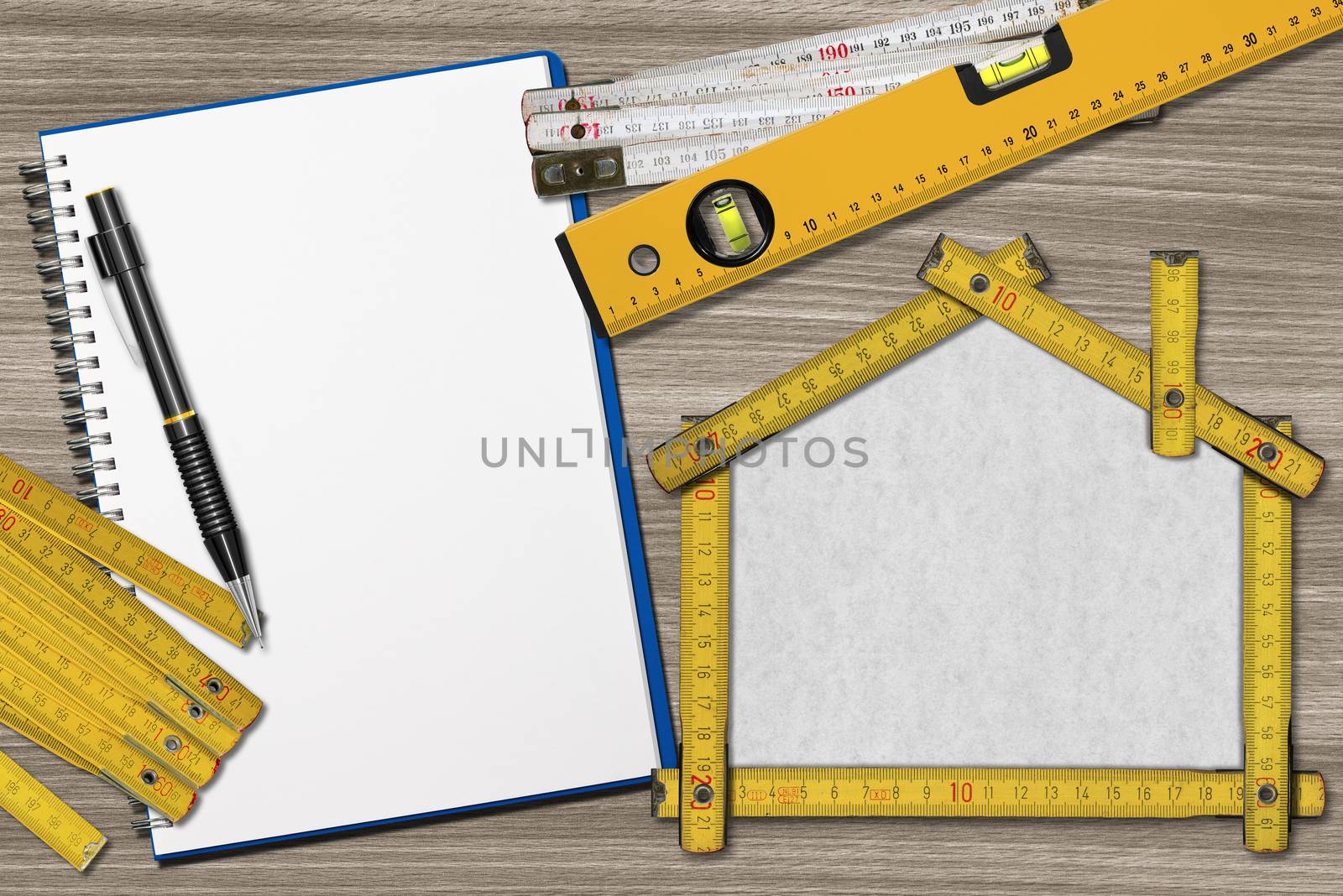 House project concept. Wooden meter ruler in the shape of house with pencil, empty notebook, two meter tools and spirit level on a wooden desk