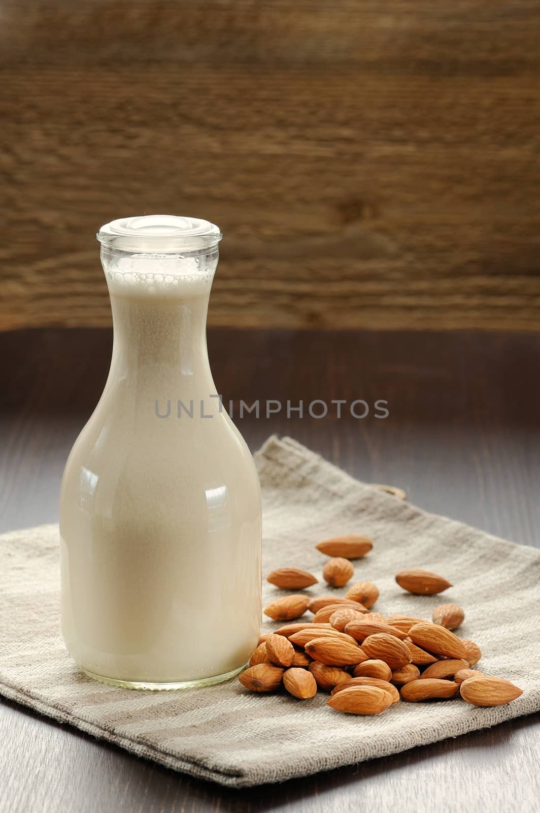 Almond milk in bottle with raw almonds on striped napkin