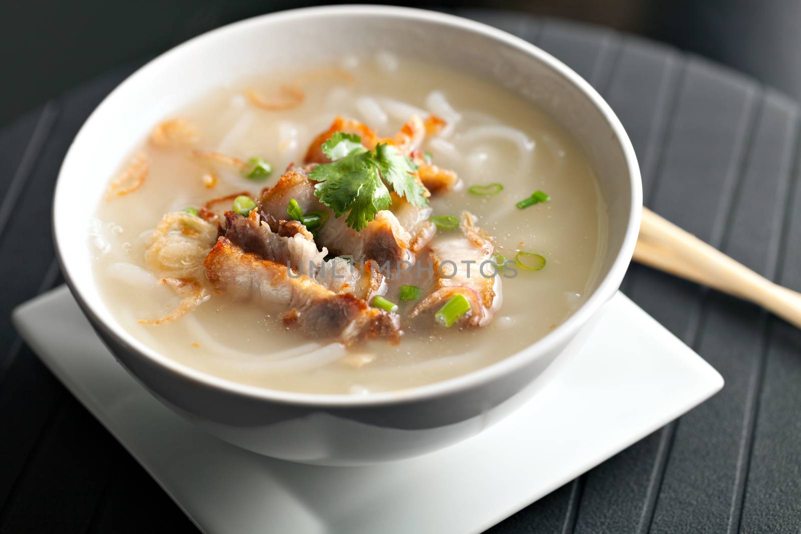 Closeup of a person eating Thai style crispy pork rice noodle soup from a bowl with chopsticks. Pineapple fried rice in the background.