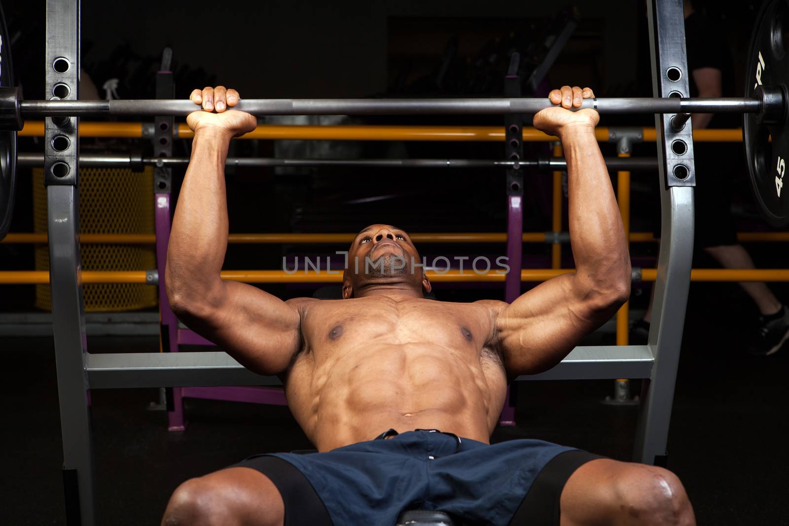 Weight lifter at the bench press lifting a barbell on an incline bench.