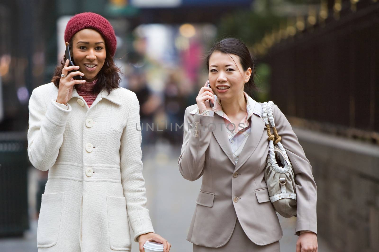 Two business women walking in the big city. One is on her cell phone.