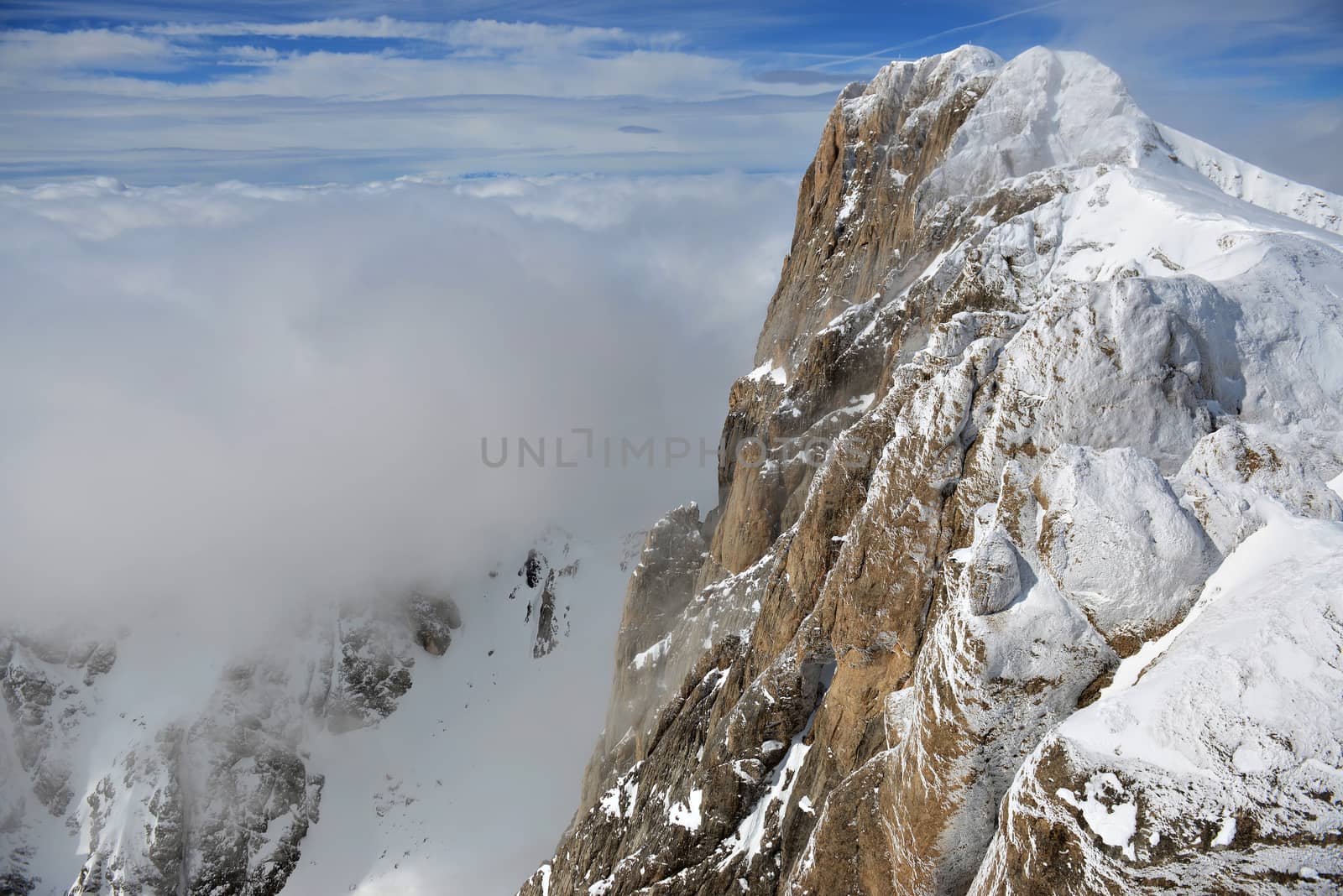 Horizontal landscape of snow and clouds covered mountain in the Alps against blue sky.