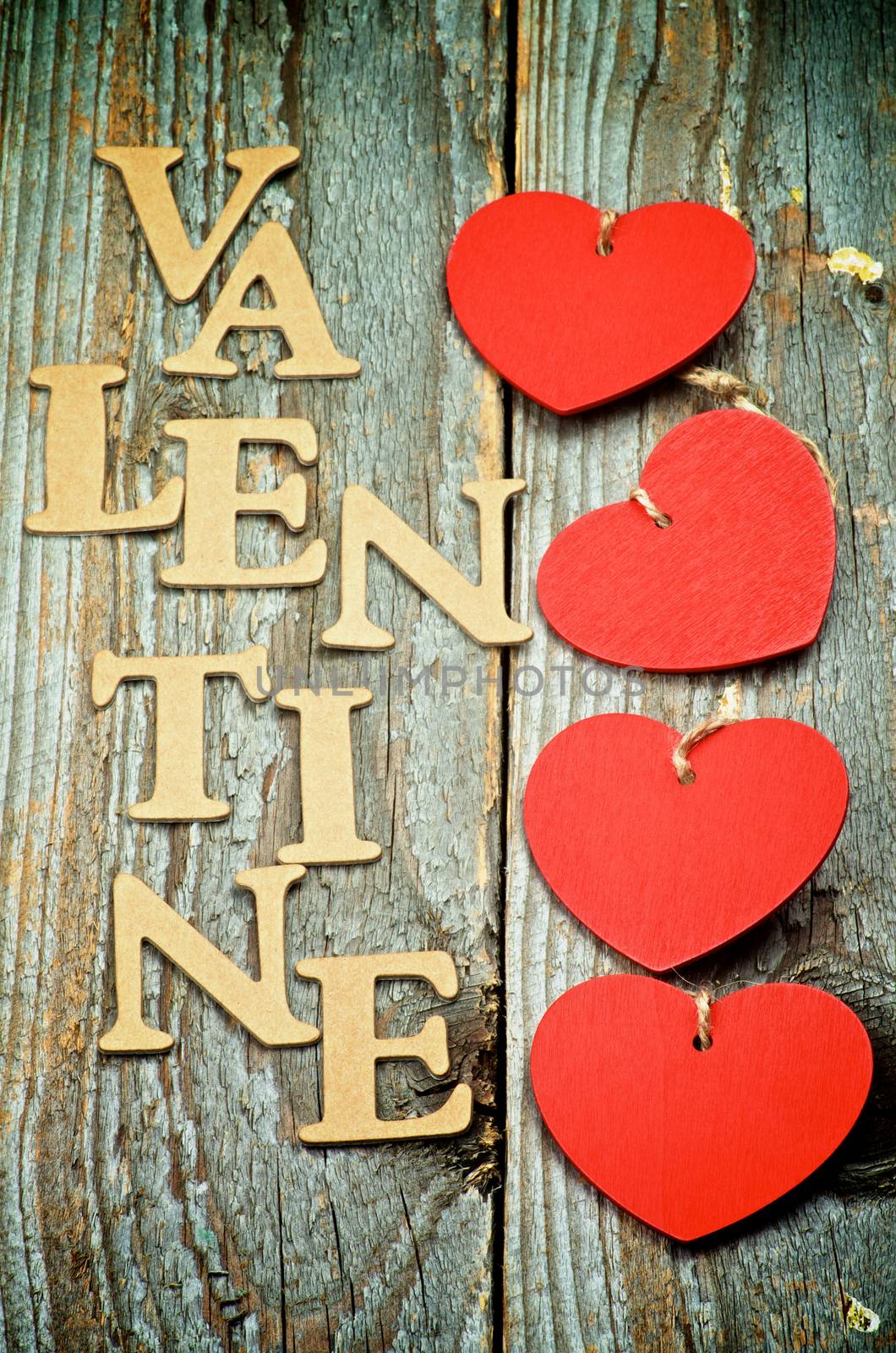 Four Red Hearts In a Row and Cardboard Words Valentine on Rustic Wooden background