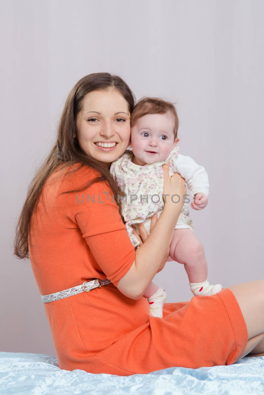 Mom with a six-month daughter sitting on bed by Madhourse