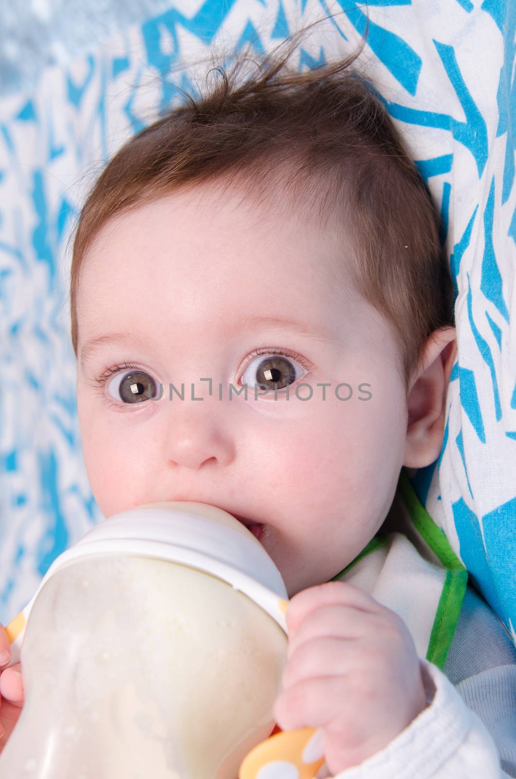 Six month old baby drinking milk from a bottle with the teat