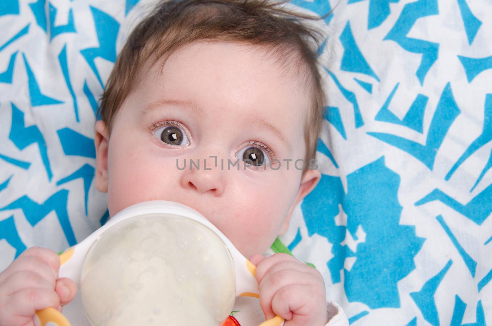Six month old baby drinking milk from a bottle with the teat