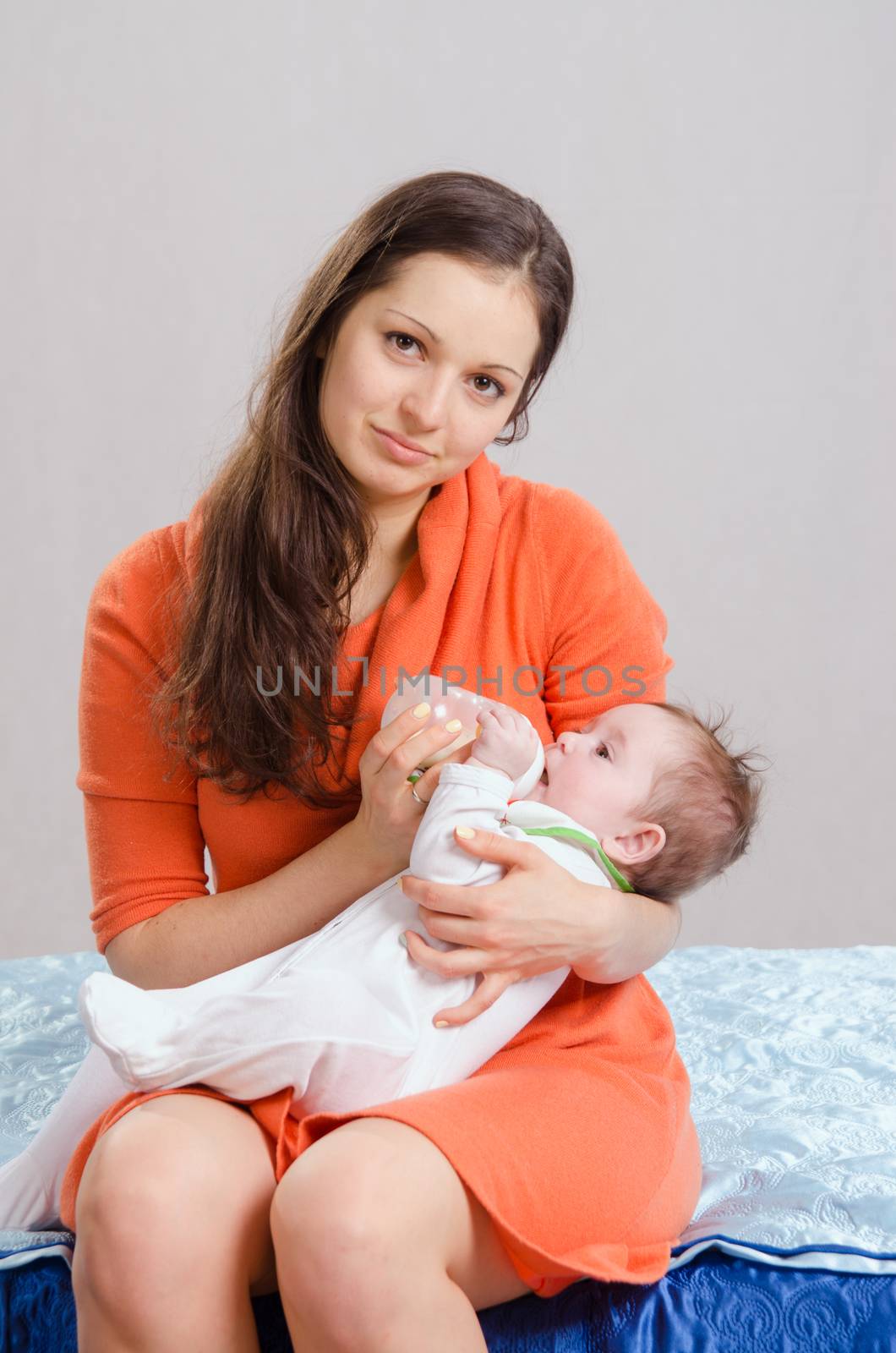 Six month old baby drinking milk from a bottle with a nipple, lying on his mother's arms