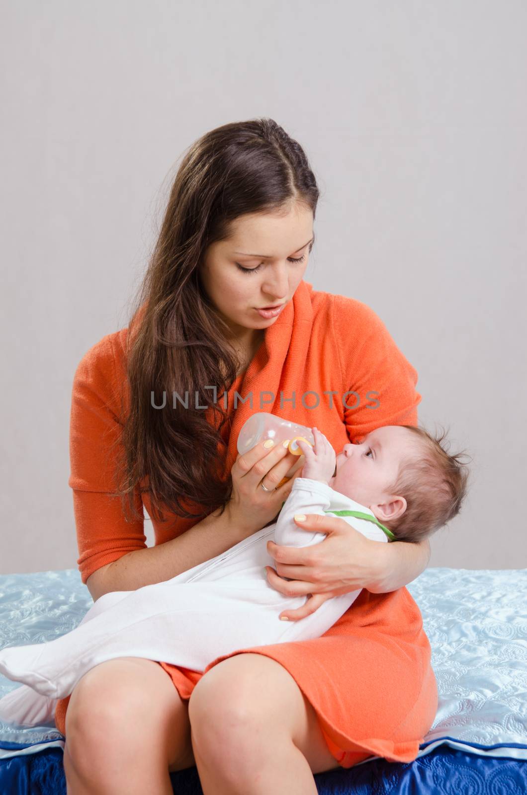 Six month old baby drinking milk from a bottle with a nipple, lying on his mother's arms