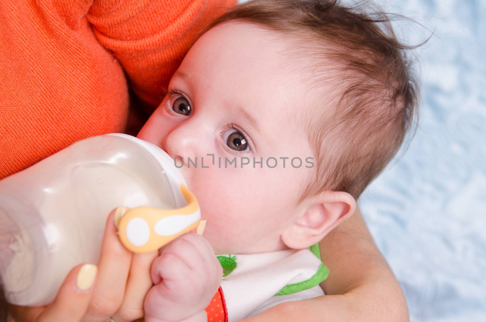 Six month old baby drinking milk from a bottle with a nipple, lying on his mother's arms