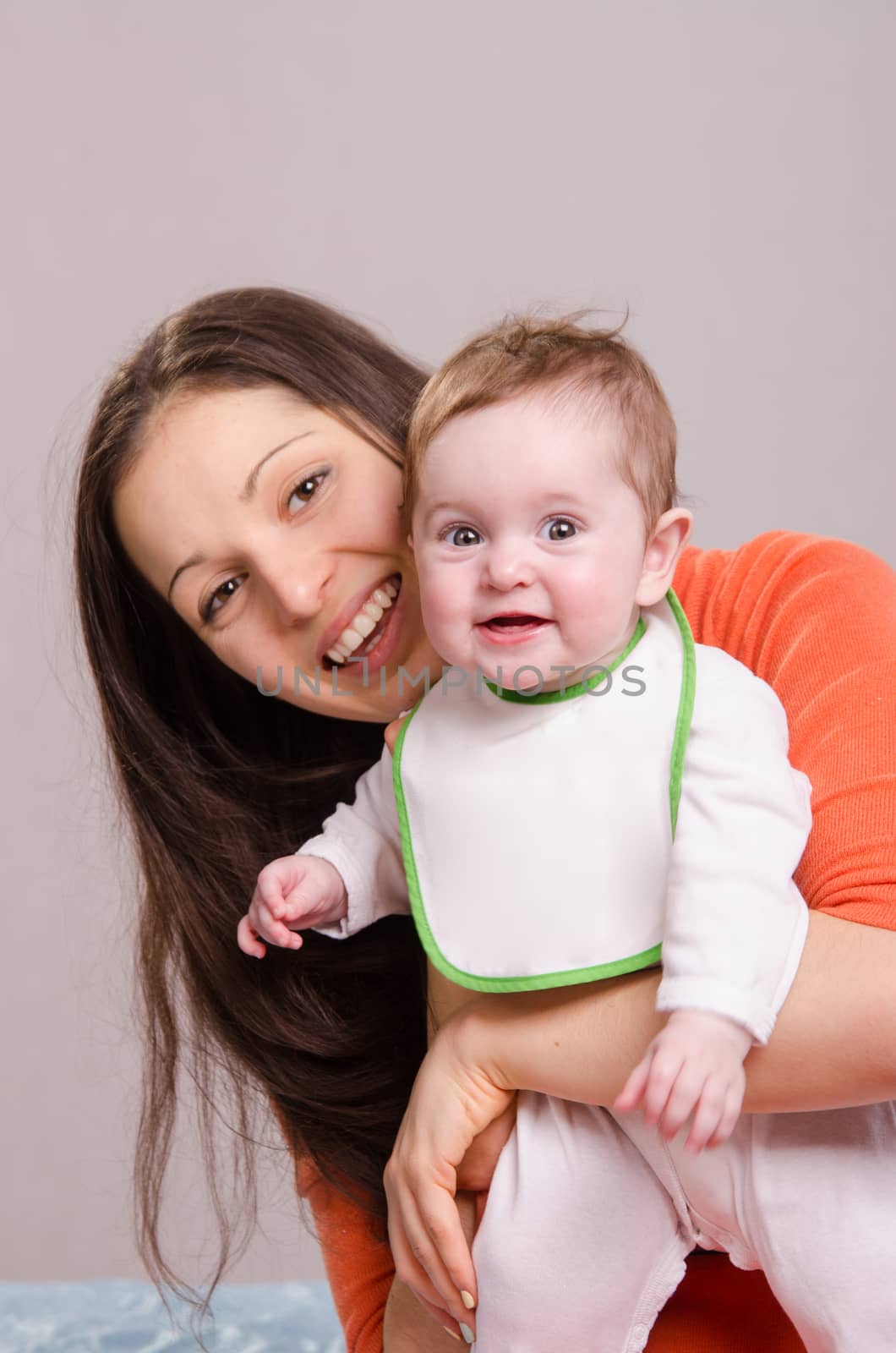 Young happy mother hugging baby girl in bib by Madhourse