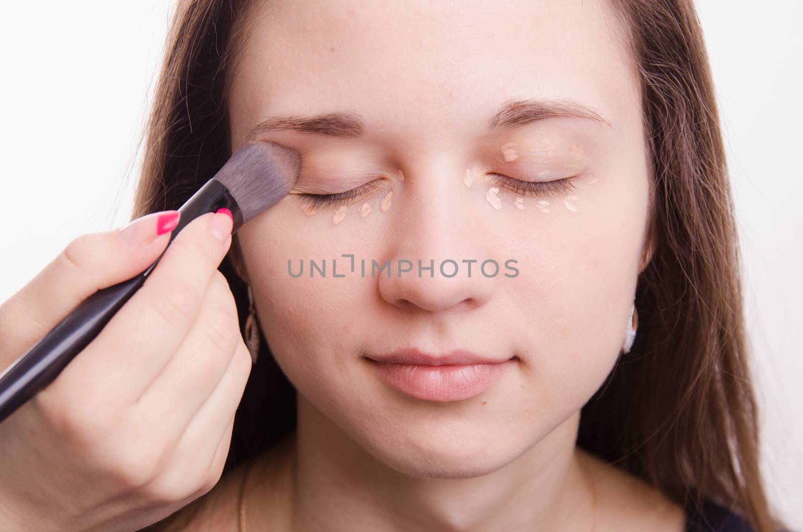 Makeup artist applies foundation of a beautiful young girl in the makeup