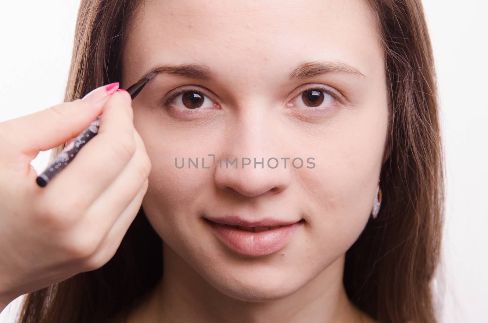 Makeup artist paints the eyebrows of a beautiful young girl in the makeup