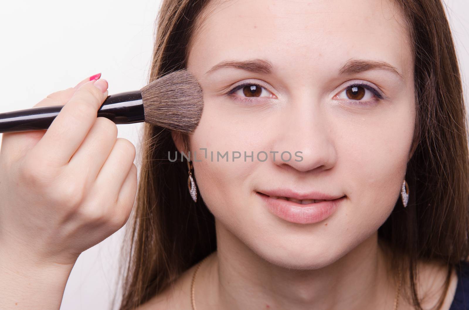 Makeup artist applies powder on the face of a beautiful young girl in the makeup