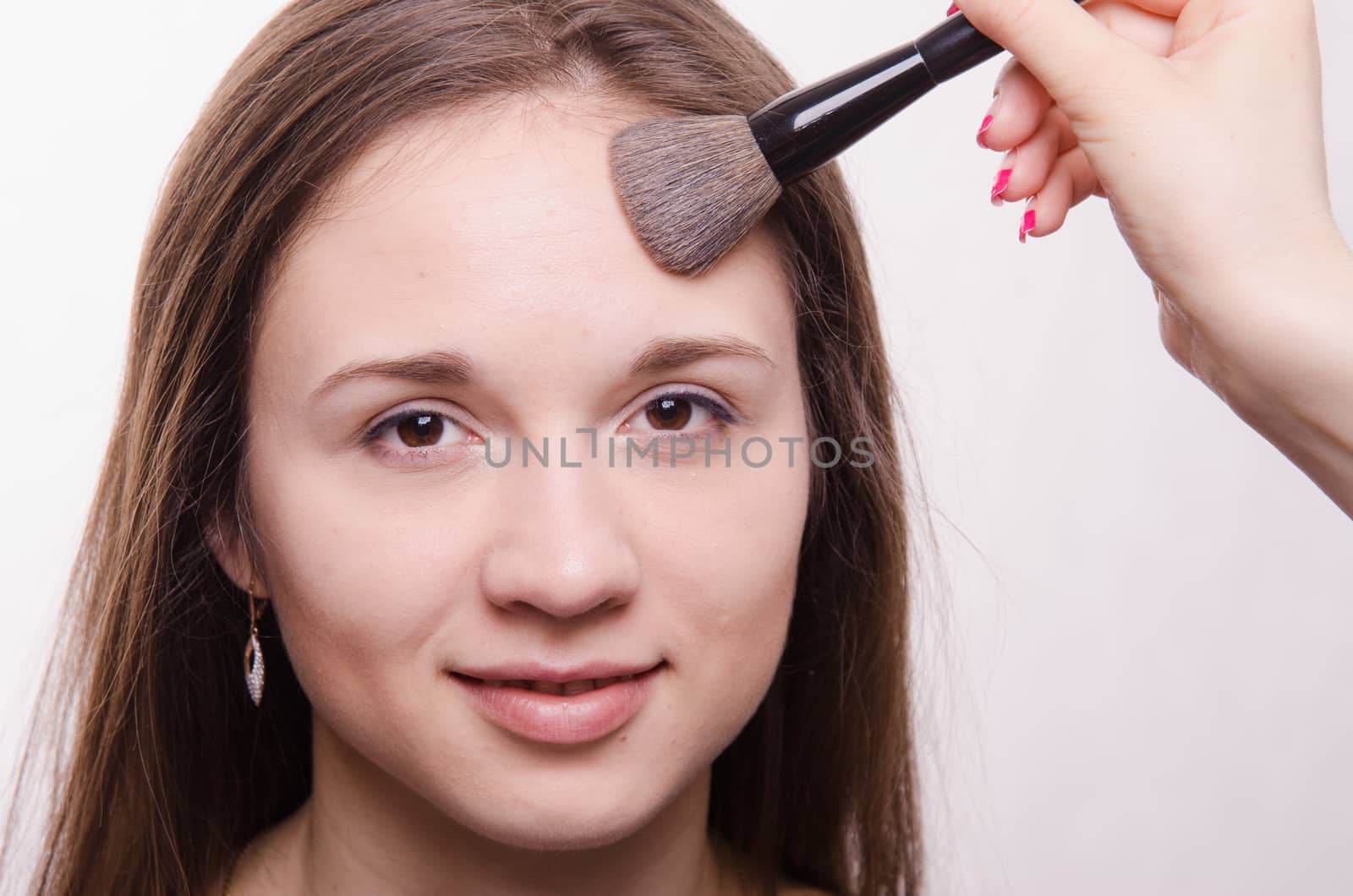 Makeup artist applies powder on the face of a beautiful young girl in the makeup