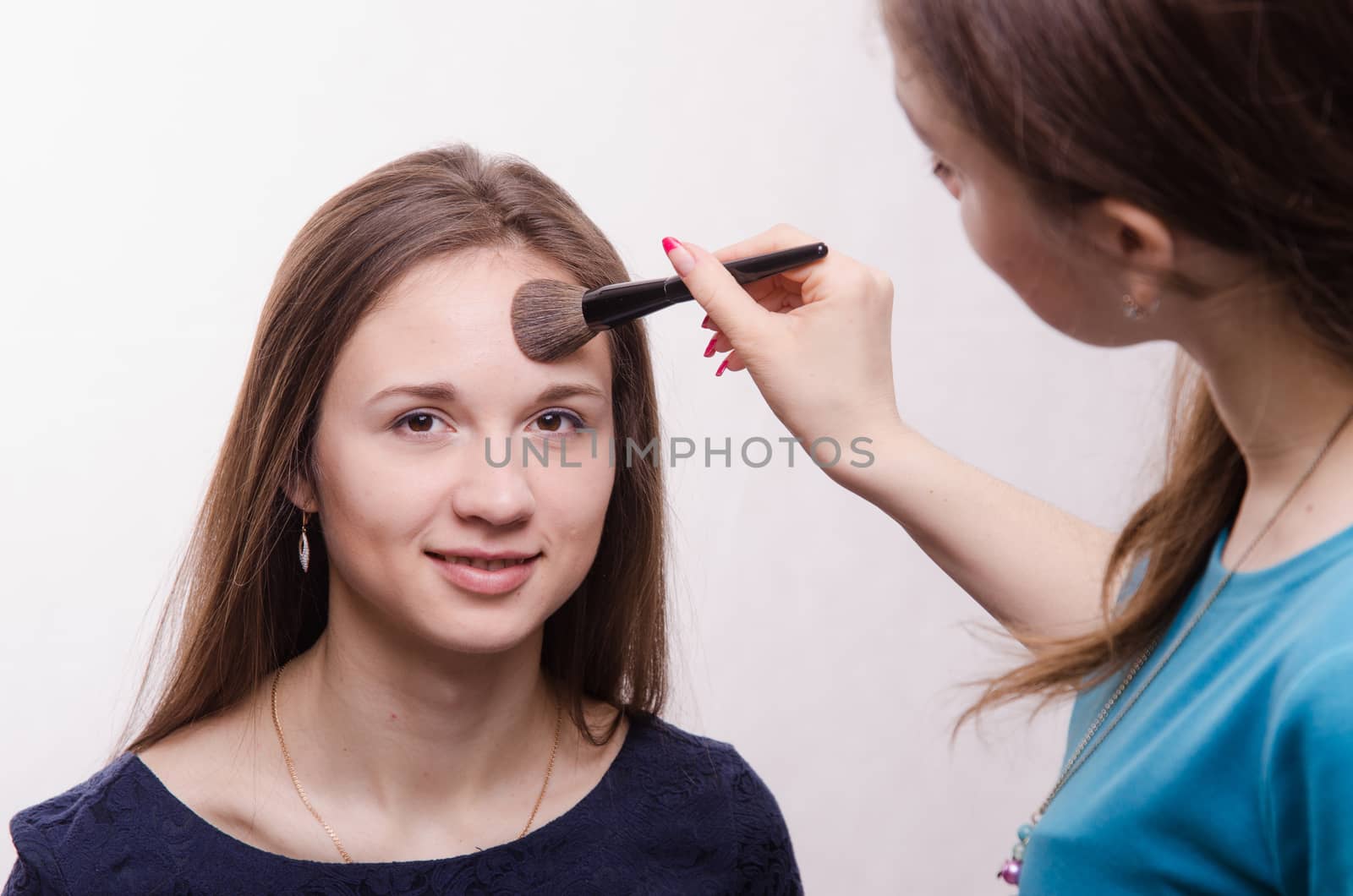 Makeup artist applies powder on the face of a beautiful young girl in the makeup