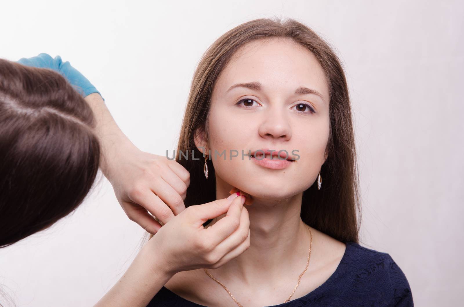 Makeup artist applies foundation of a beautiful young girl in the makeup