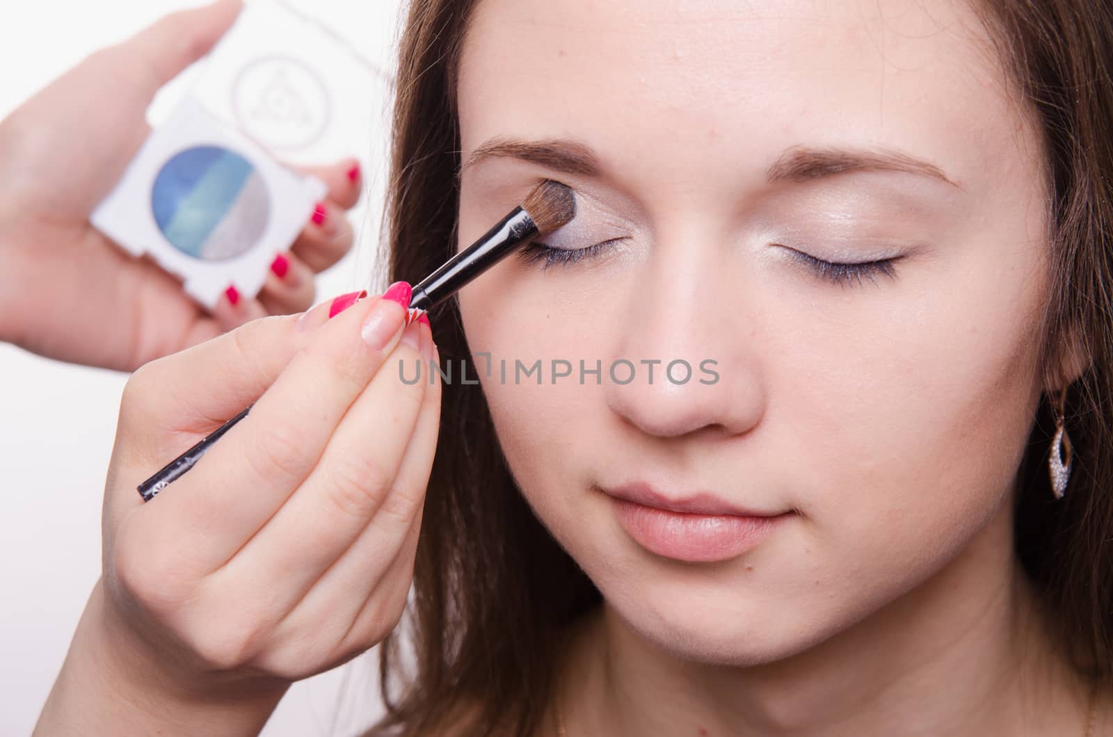 Makeup artist paints the eyelids of a beautiful young girl in the makeup