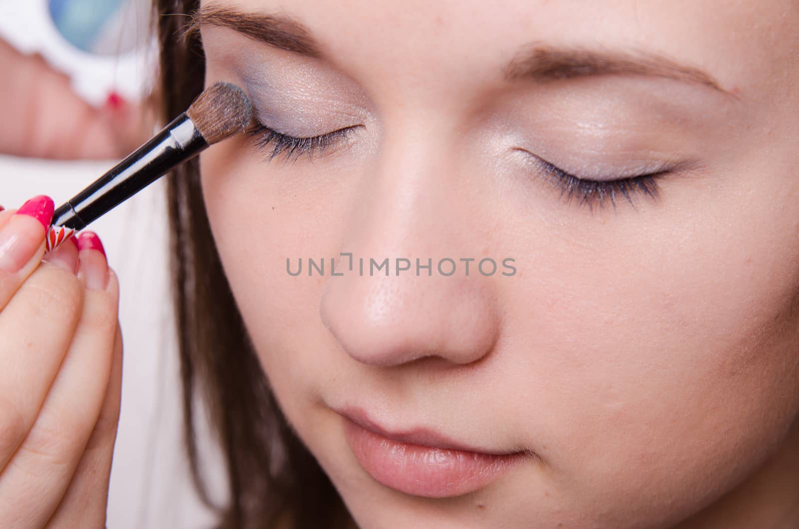Makeup artist paints the eyelids of a beautiful young girl in the makeup