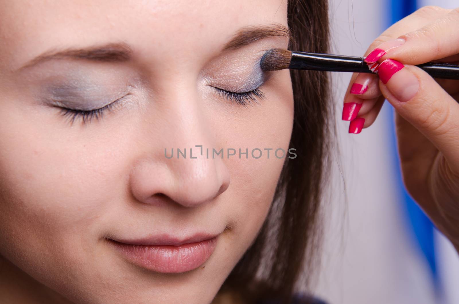 Makeup artist paints the eyelids of a beautiful young girl in the makeup