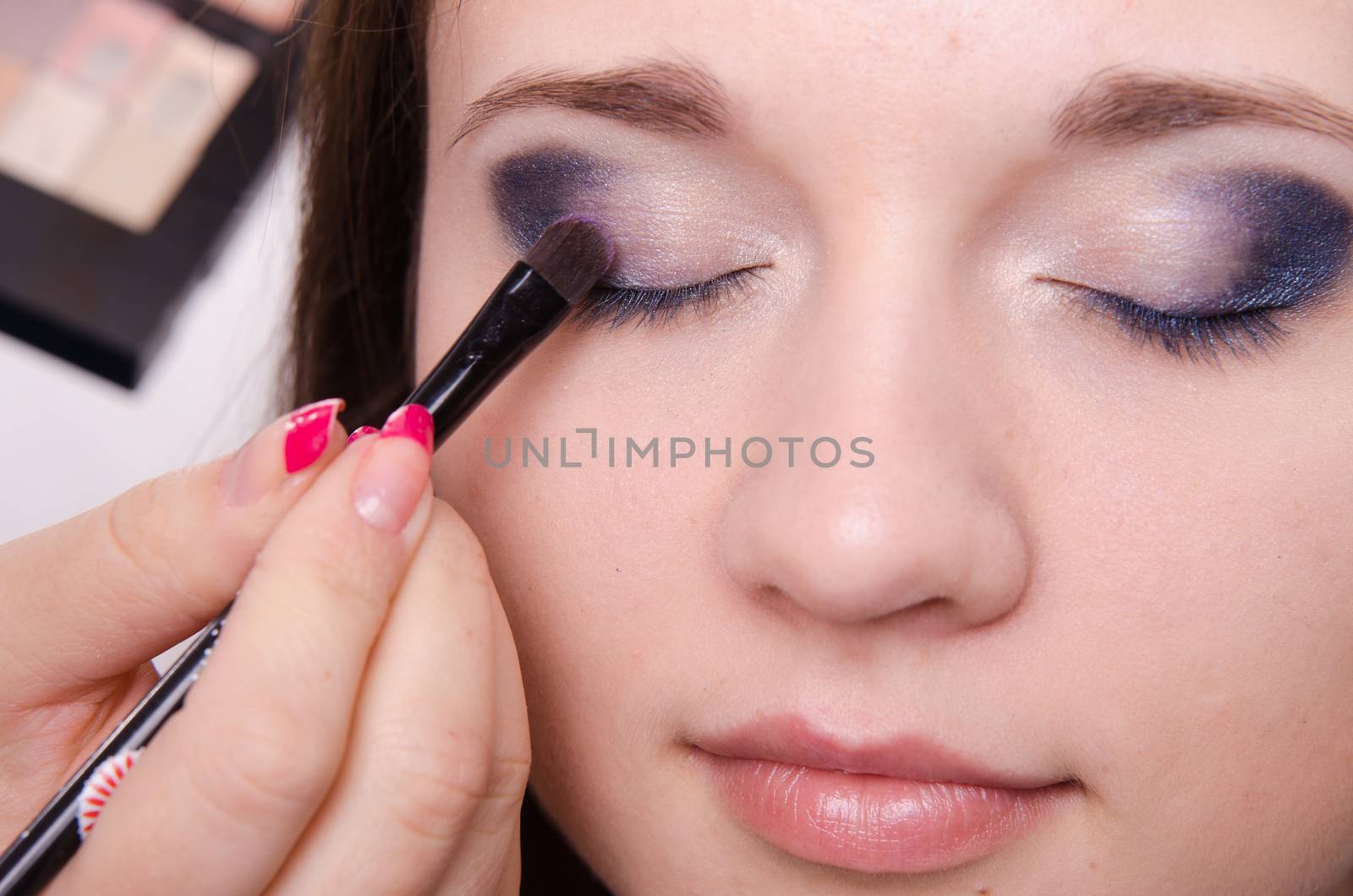 Makeup artist paints the eyelids of a beautiful young girl in the makeup