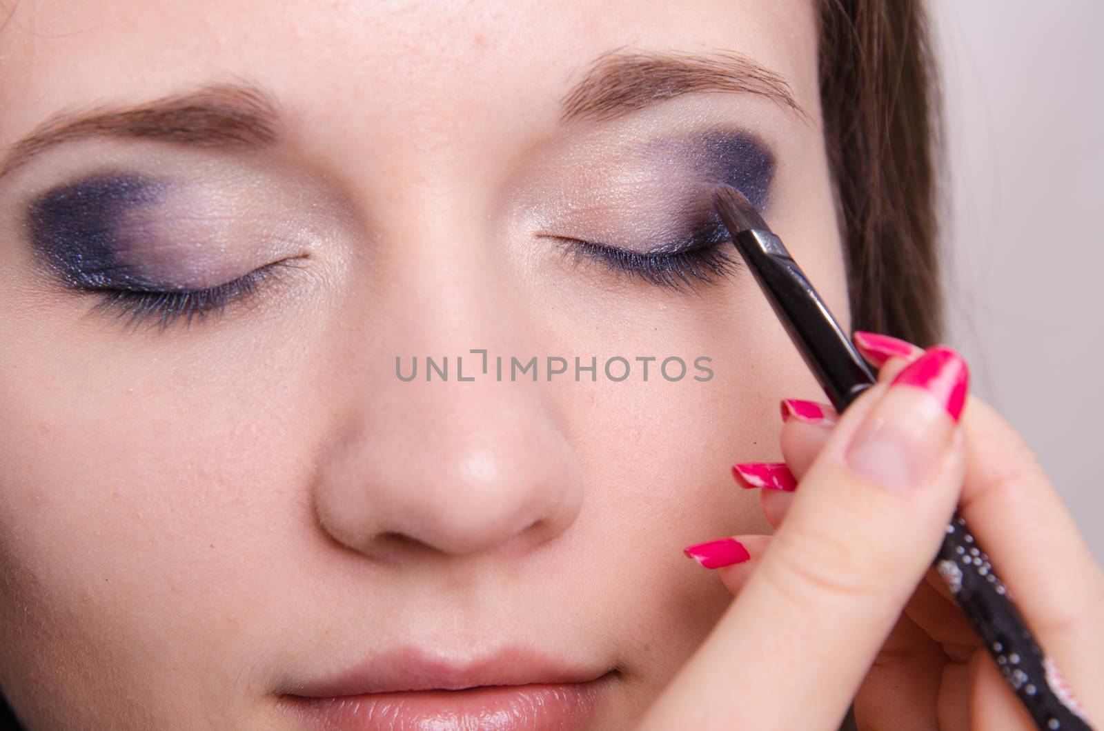 Makeup artist paints the eyelids of a beautiful young girl in the makeup