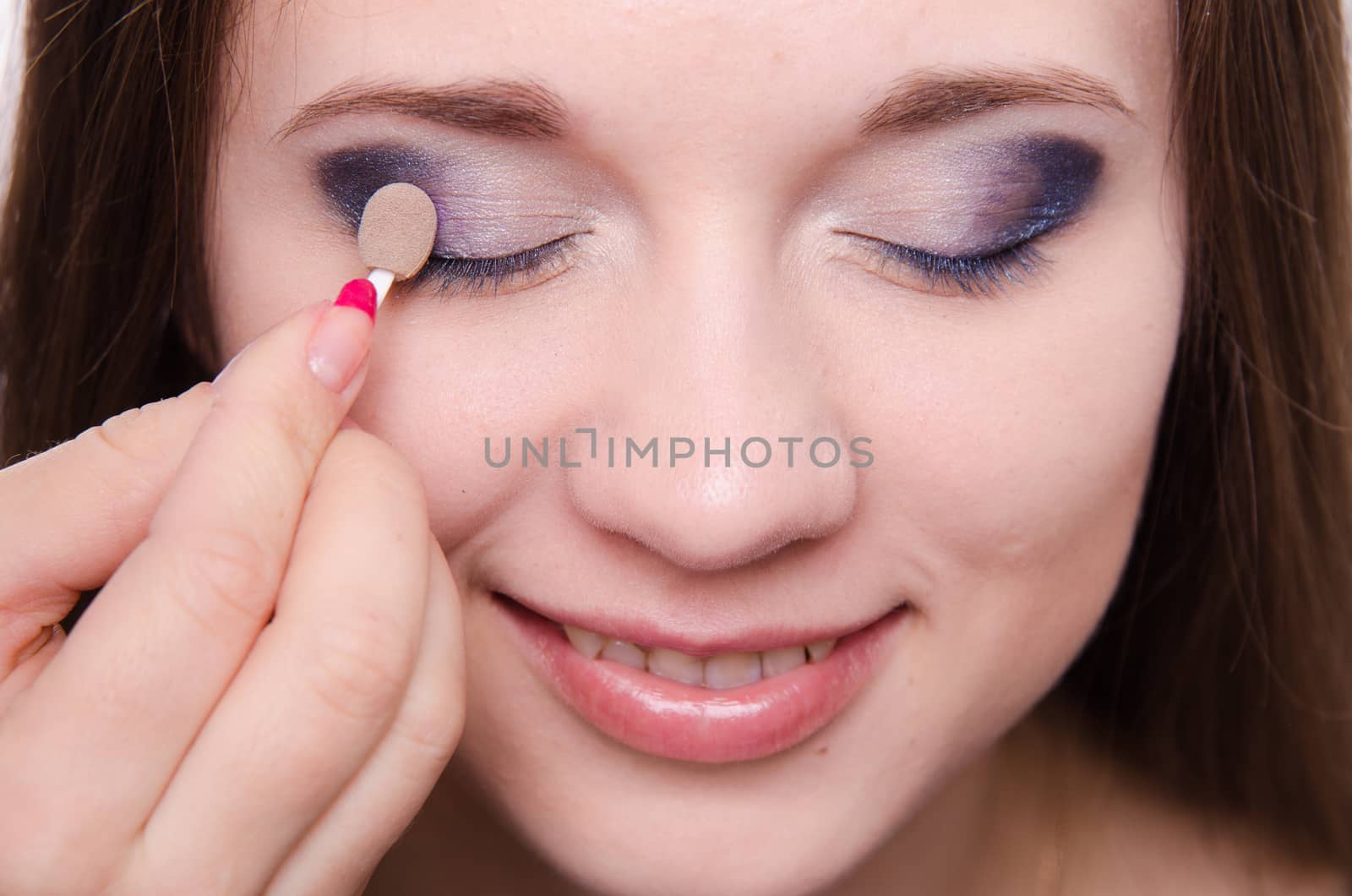 Makeup artist paints the eyelids of a beautiful young girl in the makeup