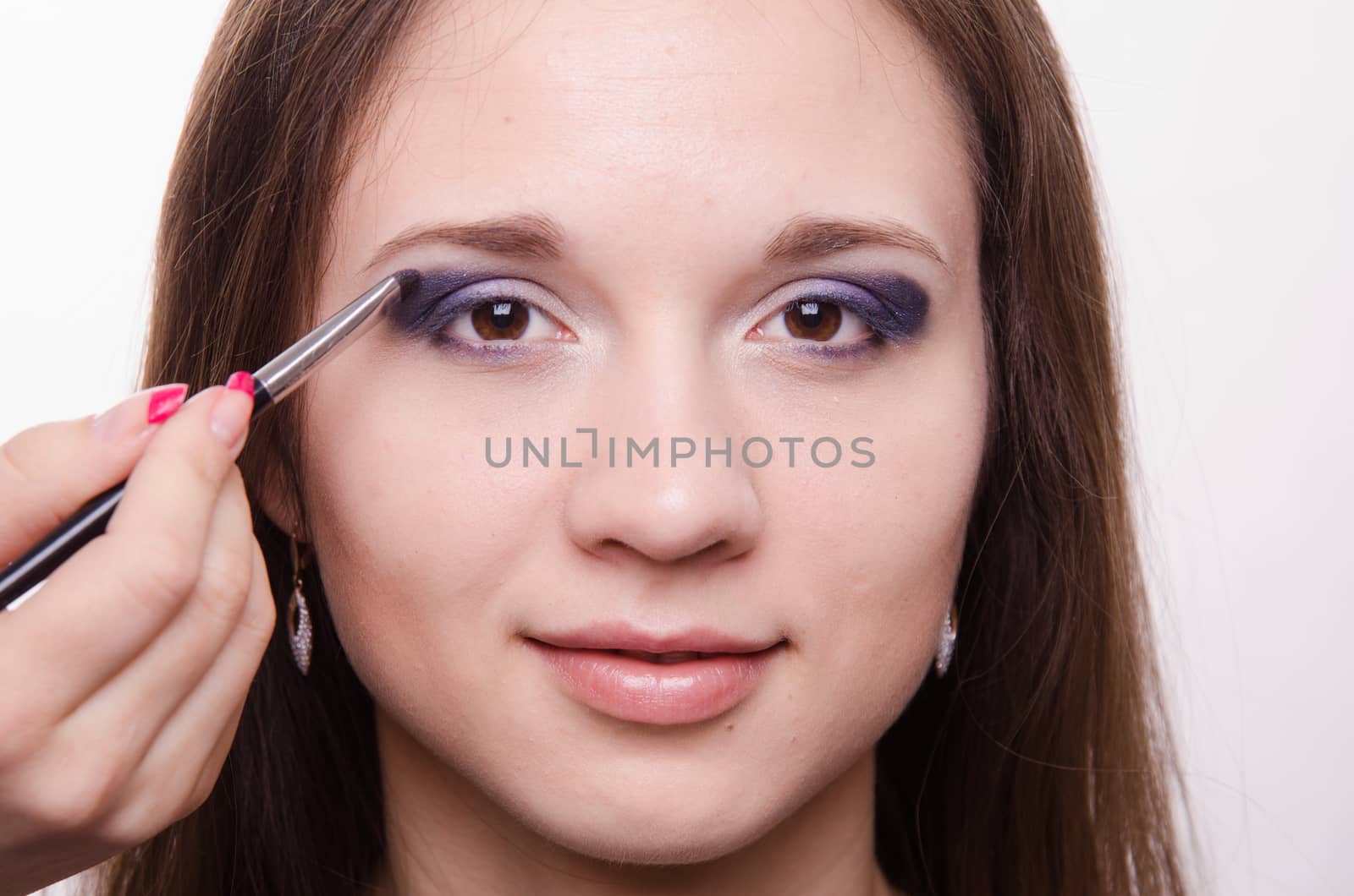 Makeup artist paints the eyelids of a beautiful young girl in the makeup