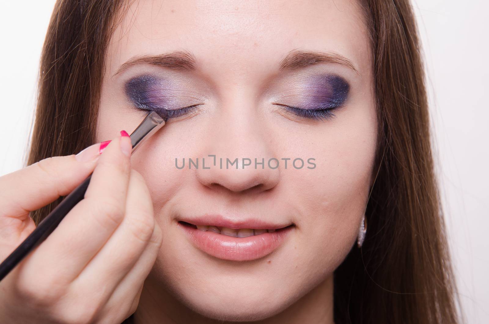 Makeup artist paints the eyelids of a beautiful young girl in the makeup