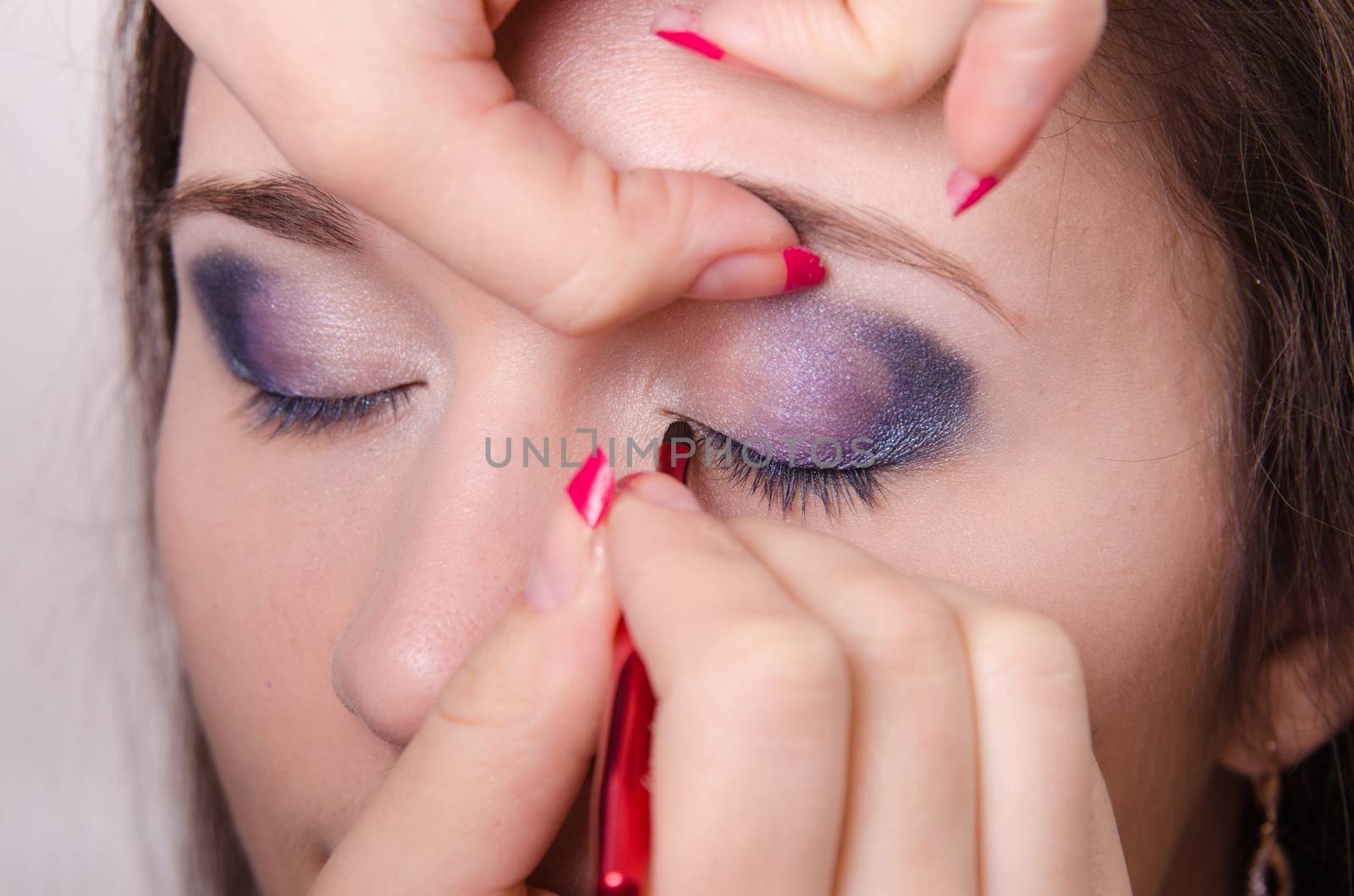 Makeup artist paints eyelashes of a beautiful young girl in the makeup