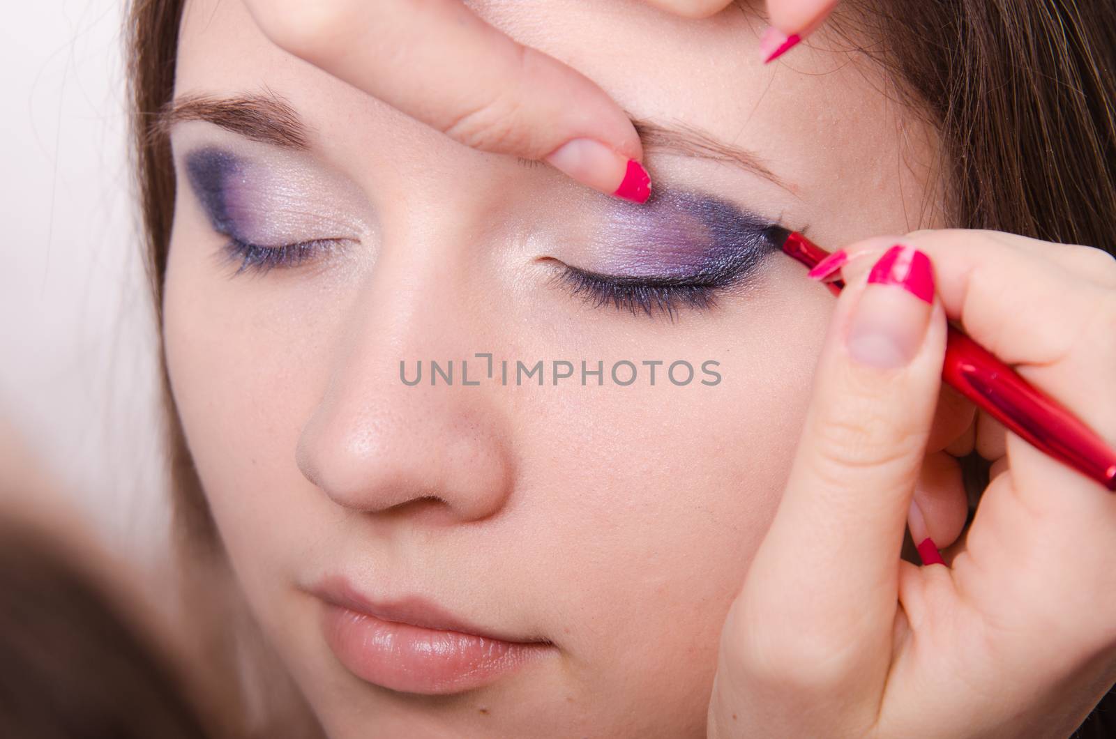 Makeup artist draws arrows beautiful young girl in the makeup