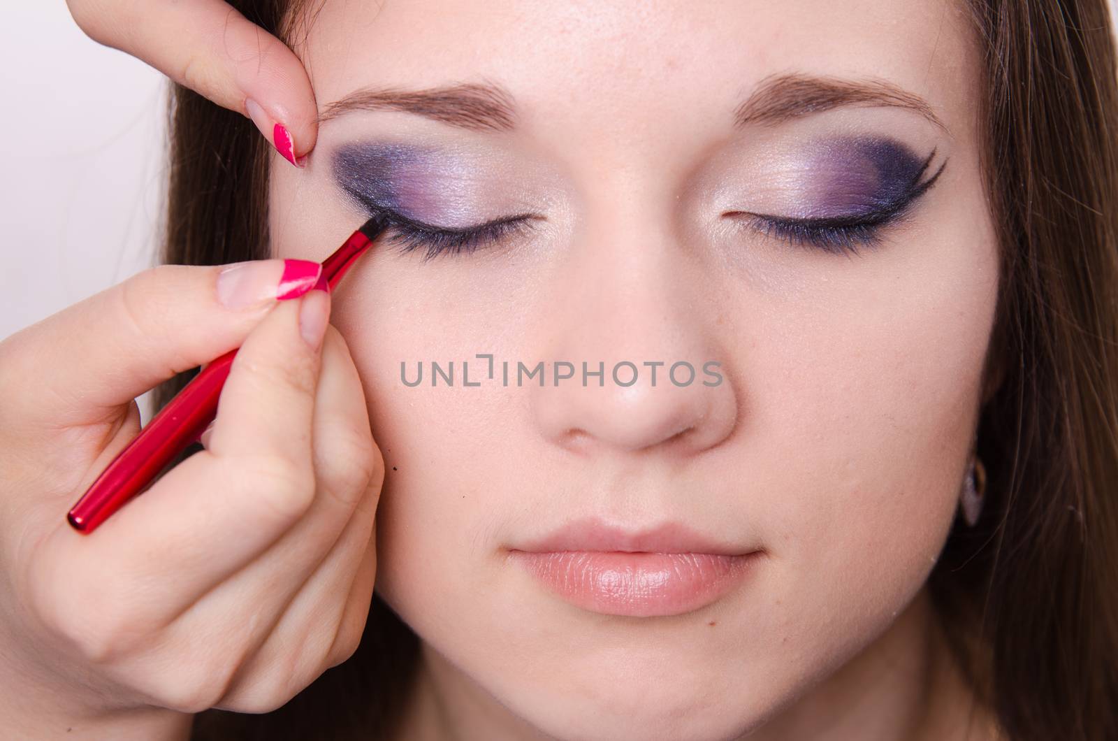Makeup artist draws arrows beautiful young girl in the makeup