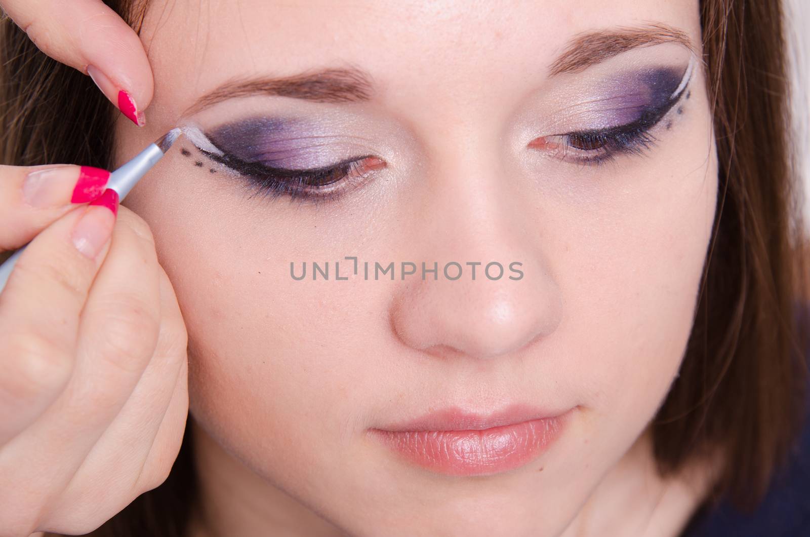 Makeup artist draws arrows beautiful young girl in the makeup