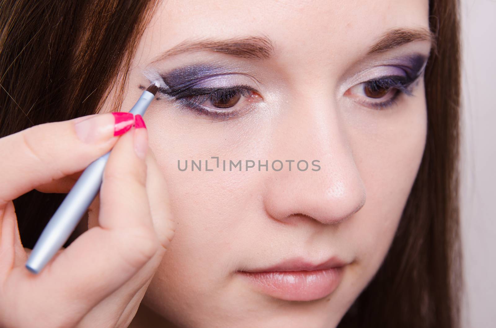 Makeup artist draws arrows beautiful young girl in the makeup
