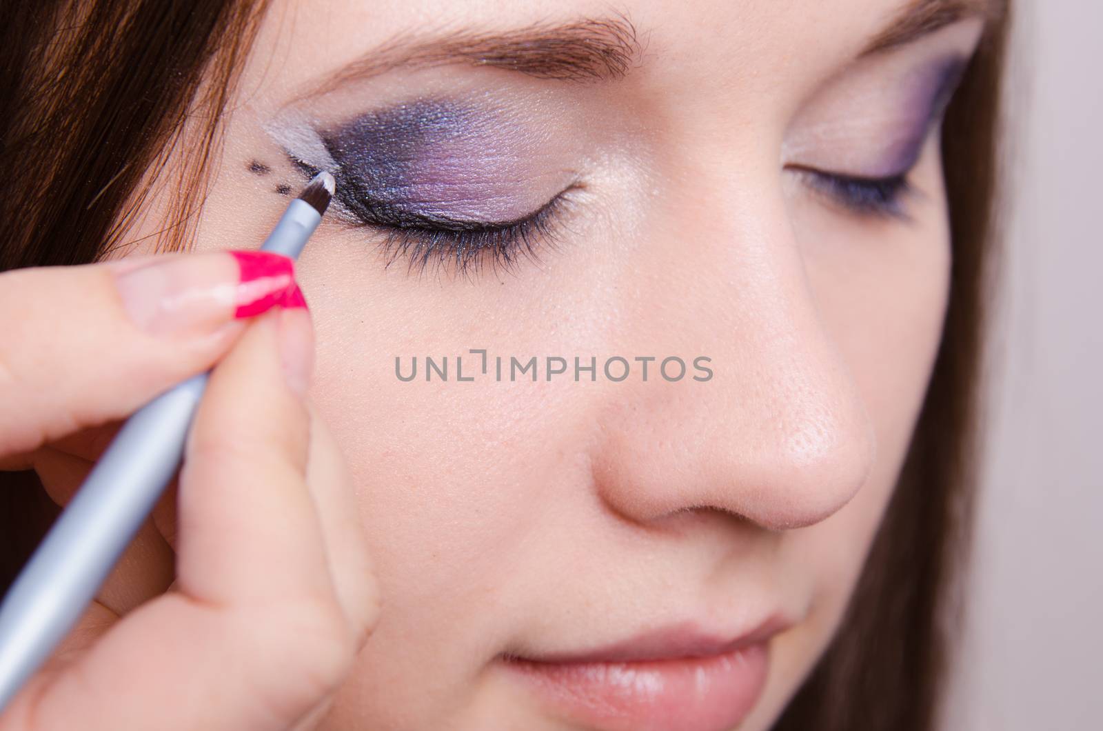 Makeup artist draws arrows beautiful young girl in the makeup