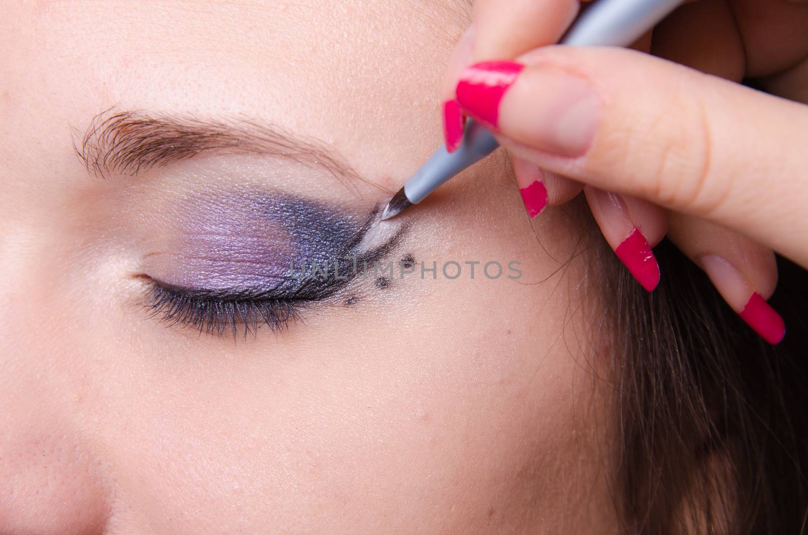 Makeup artist draws arrows beautiful young girl in the makeup
