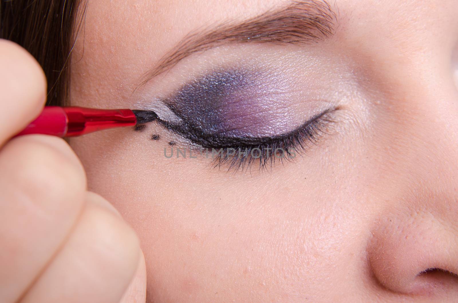 Makeup artist draws arrows beautiful young girl in the makeup