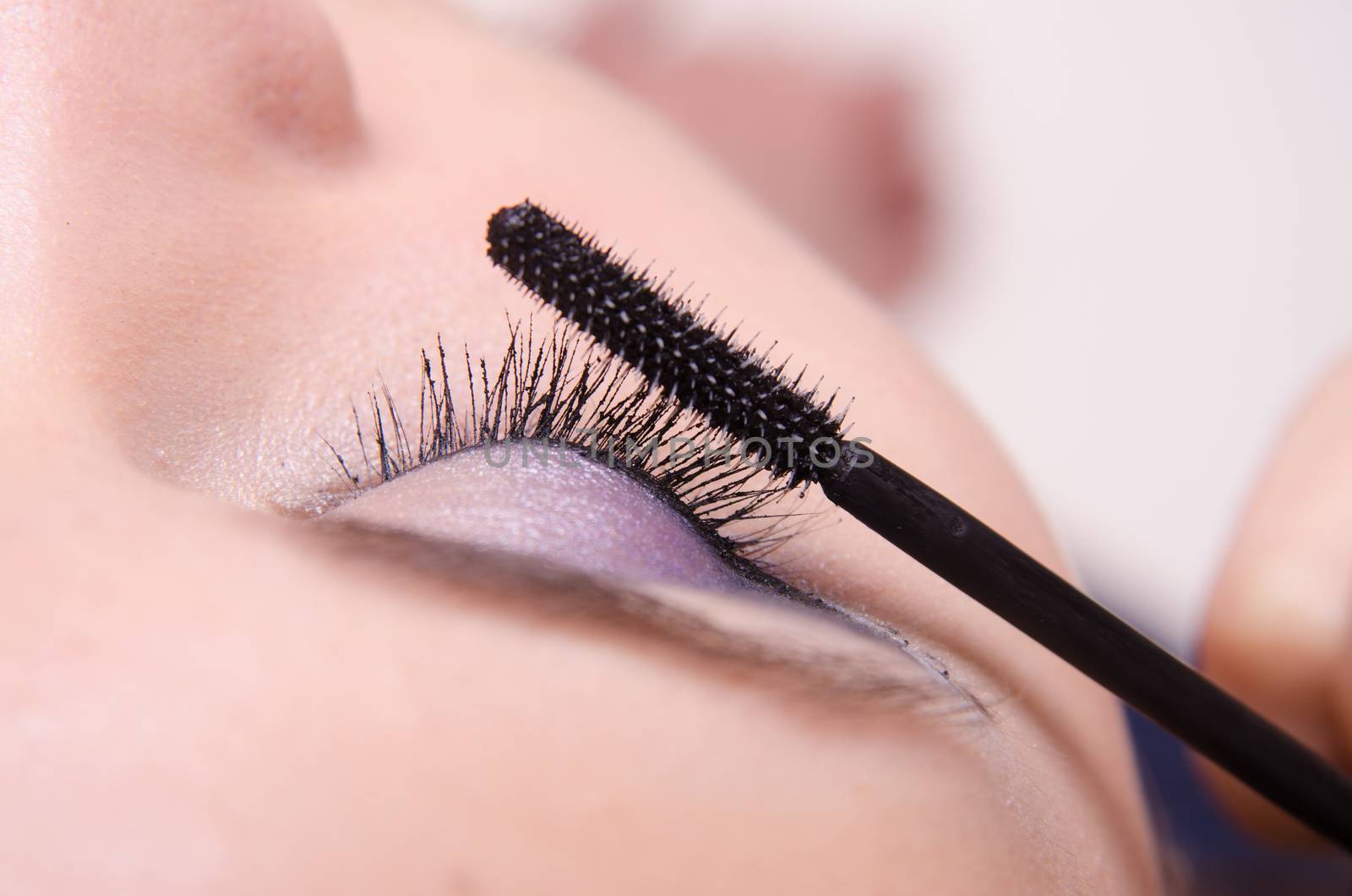 Makeup artist paints eyelashes of a beautiful young girl in the makeup