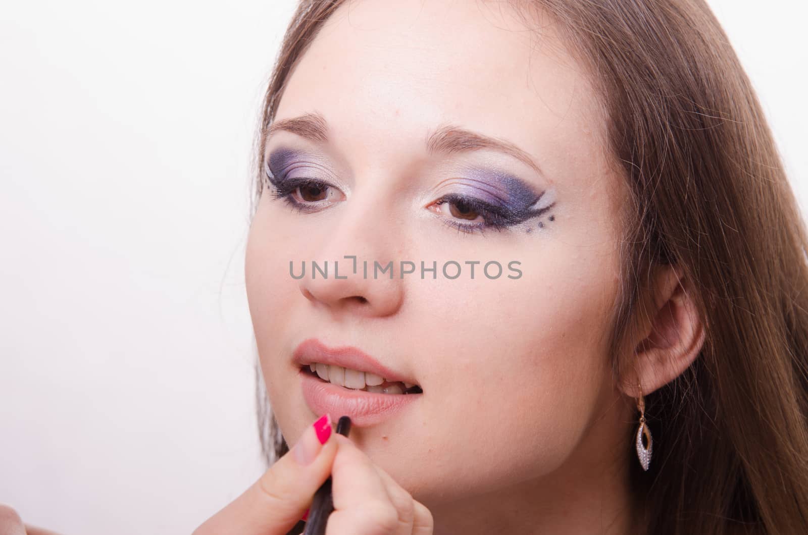 Makeup artist paints her lips a beautiful young girl in the makeup