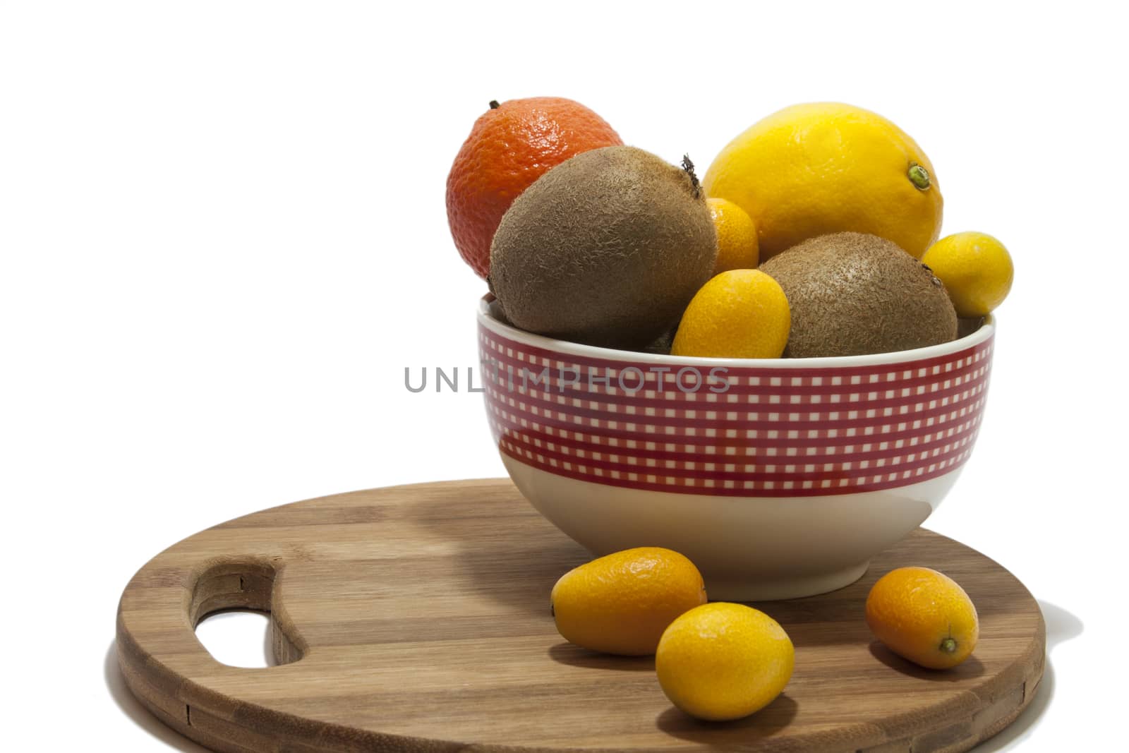 Fruit arrangement in the bowl and on the kitchen wooden board. Lemon, kumquat, kiwi and tangerine in the bowl and on the kitchen wooden board.