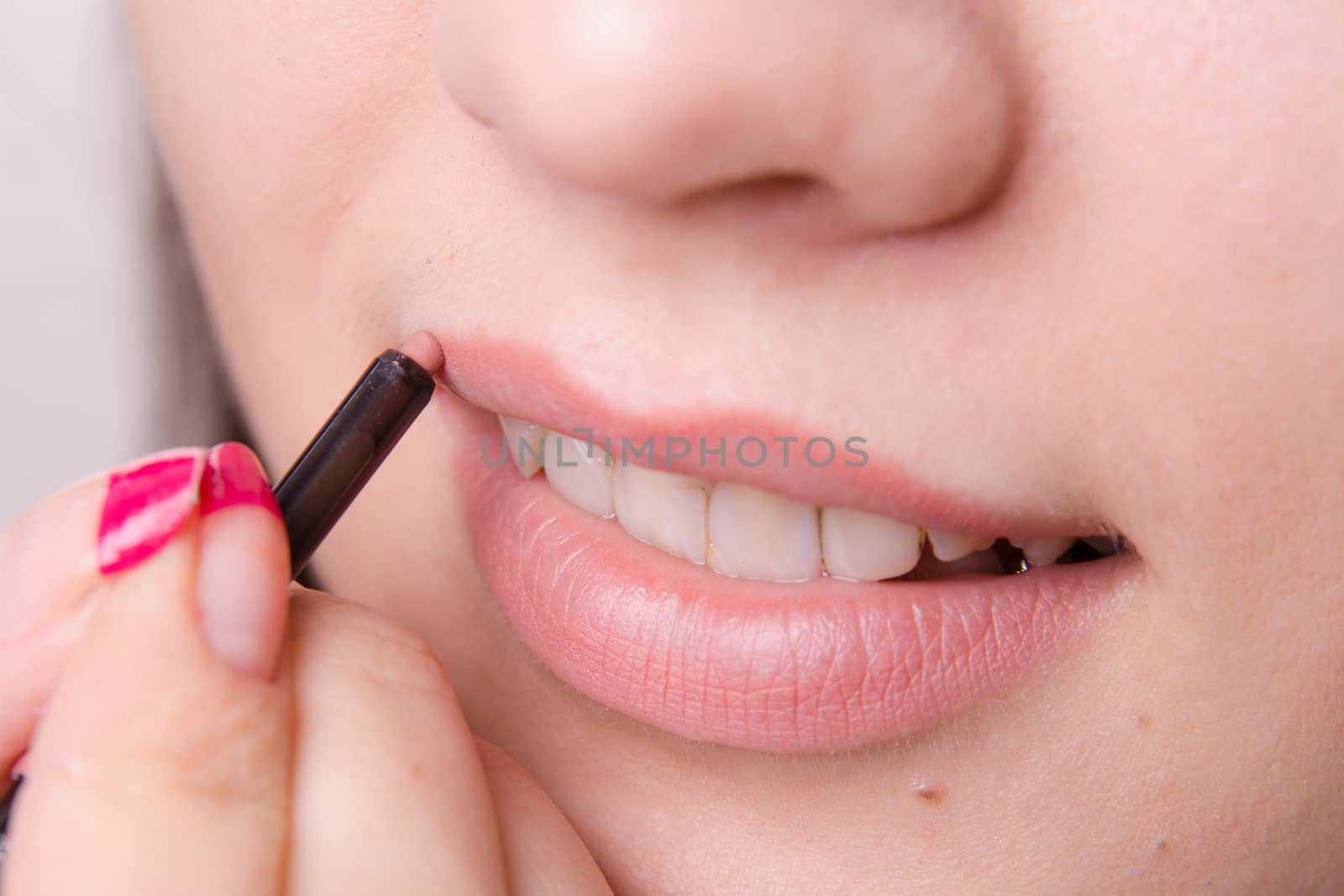 Makeup artist paints her lips a beautiful young girl in the makeup