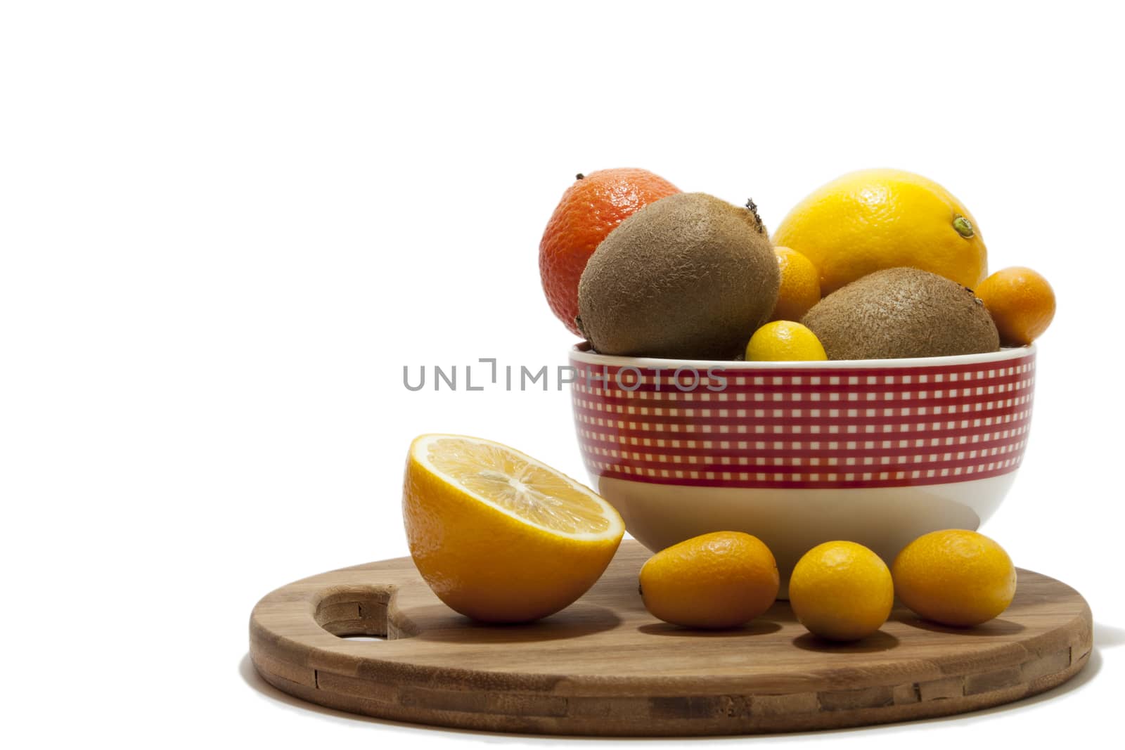 Fruit arrangement in the bowl and on the kitchen wooden board. Lemon, kumquat, kiwi and tangerine in the bowl and on the kitchen wooden board.