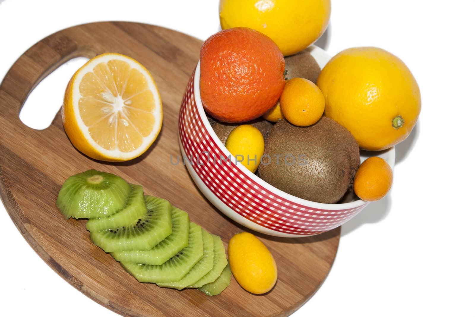 Fruit arrangement in the bowl and on the kitchen wooden board. Lemon, kumquat, kiwi and tangerine in the bowl and on the kitchen wooden board.