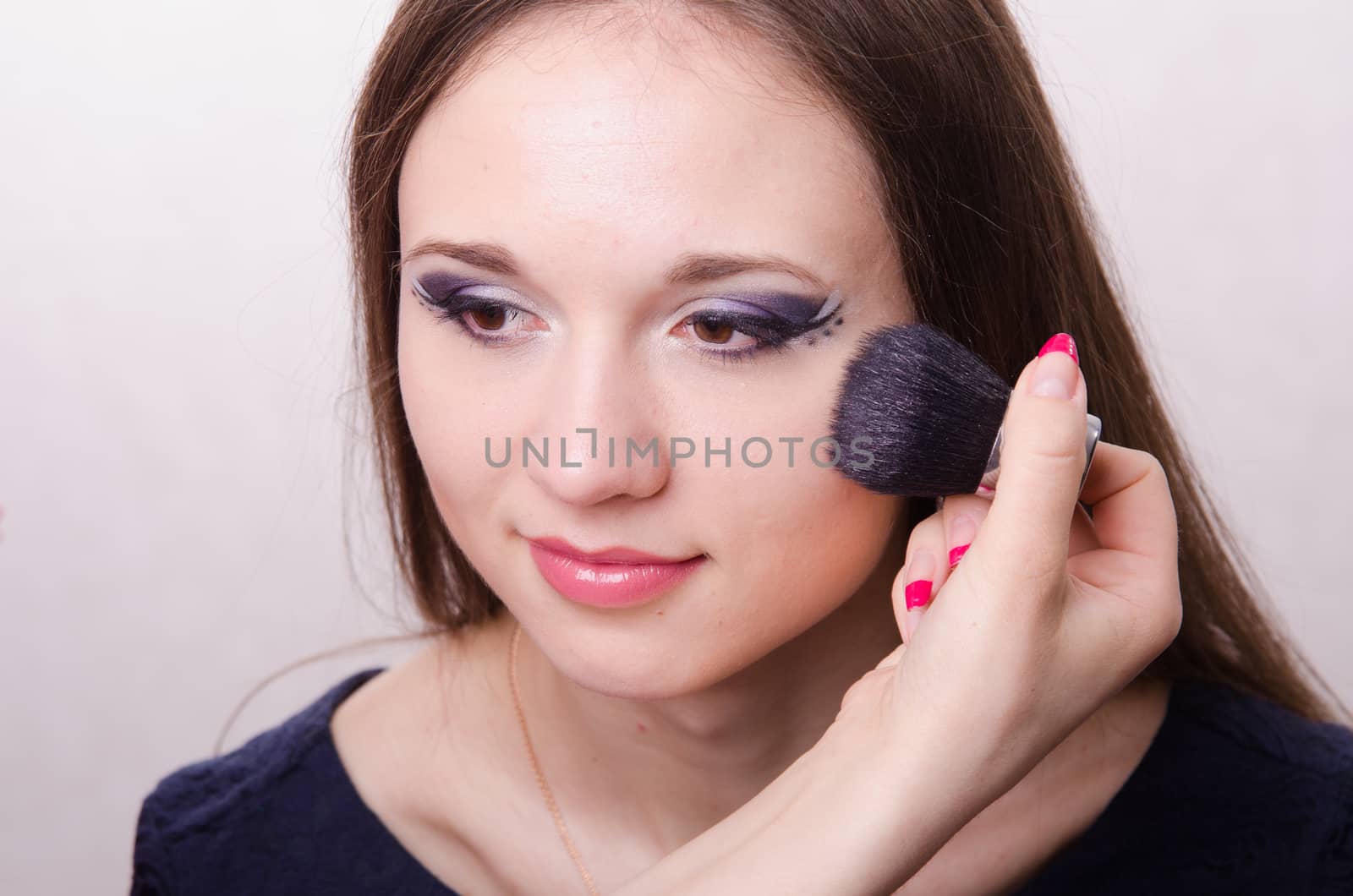Makeup artist brush powder gets on the face of a beautiful young girl in the makeup