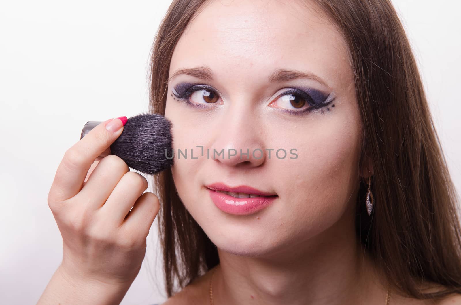 Makeup artist brush powder gets on the face of a beautiful young girl in the makeup