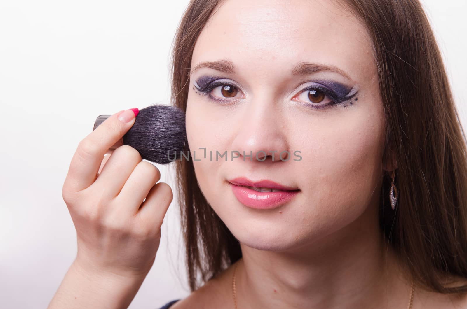 Makeup artist brush powder gets on the face of a beautiful young girl in the makeup