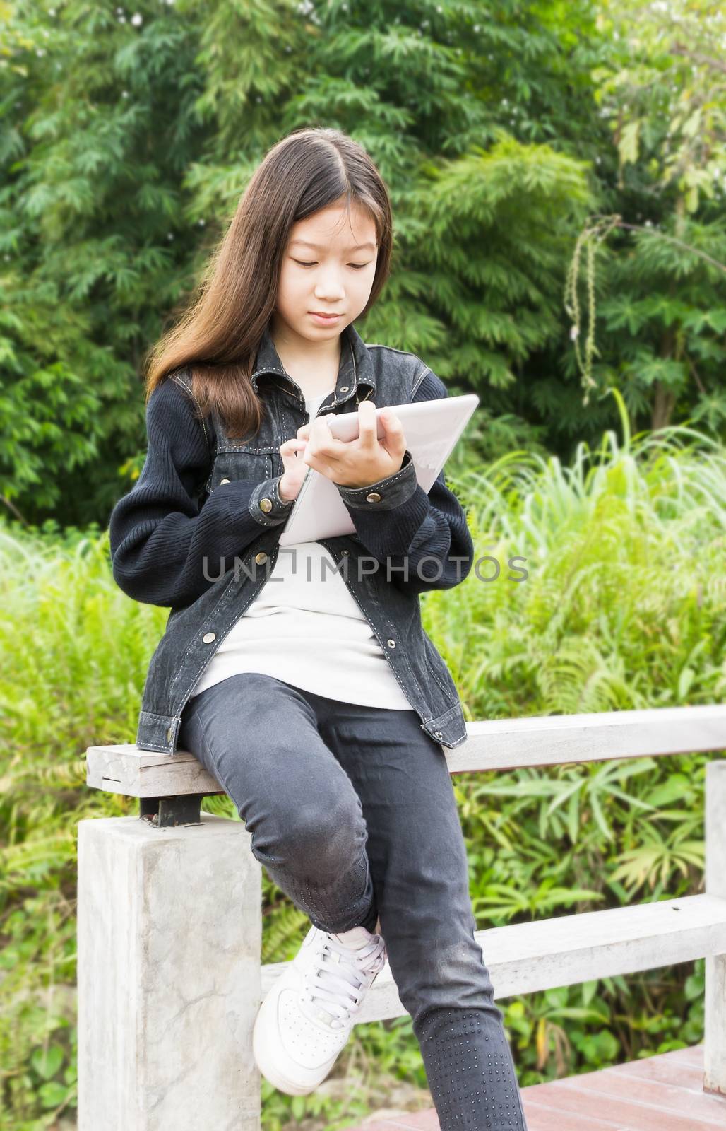 Beautiful Asian young girl using tablet computer in park