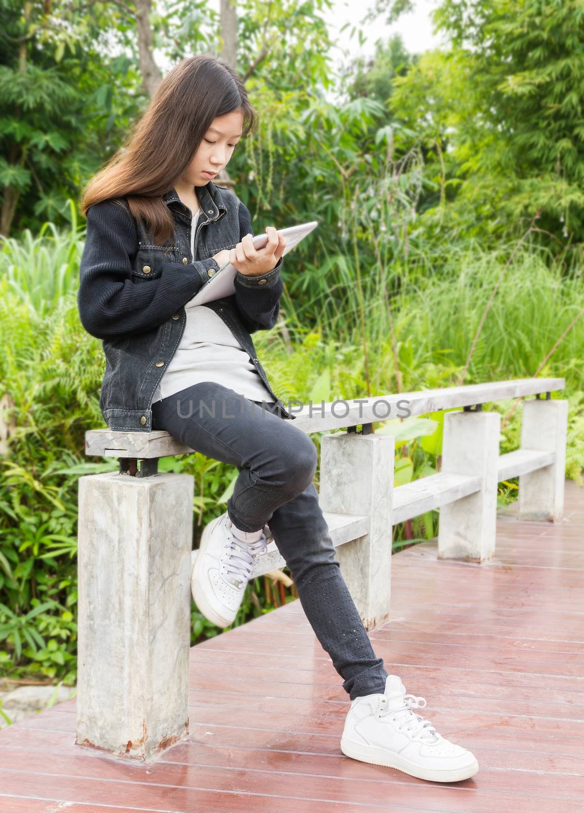 Beautiful Asian young girl using tablet computer in park