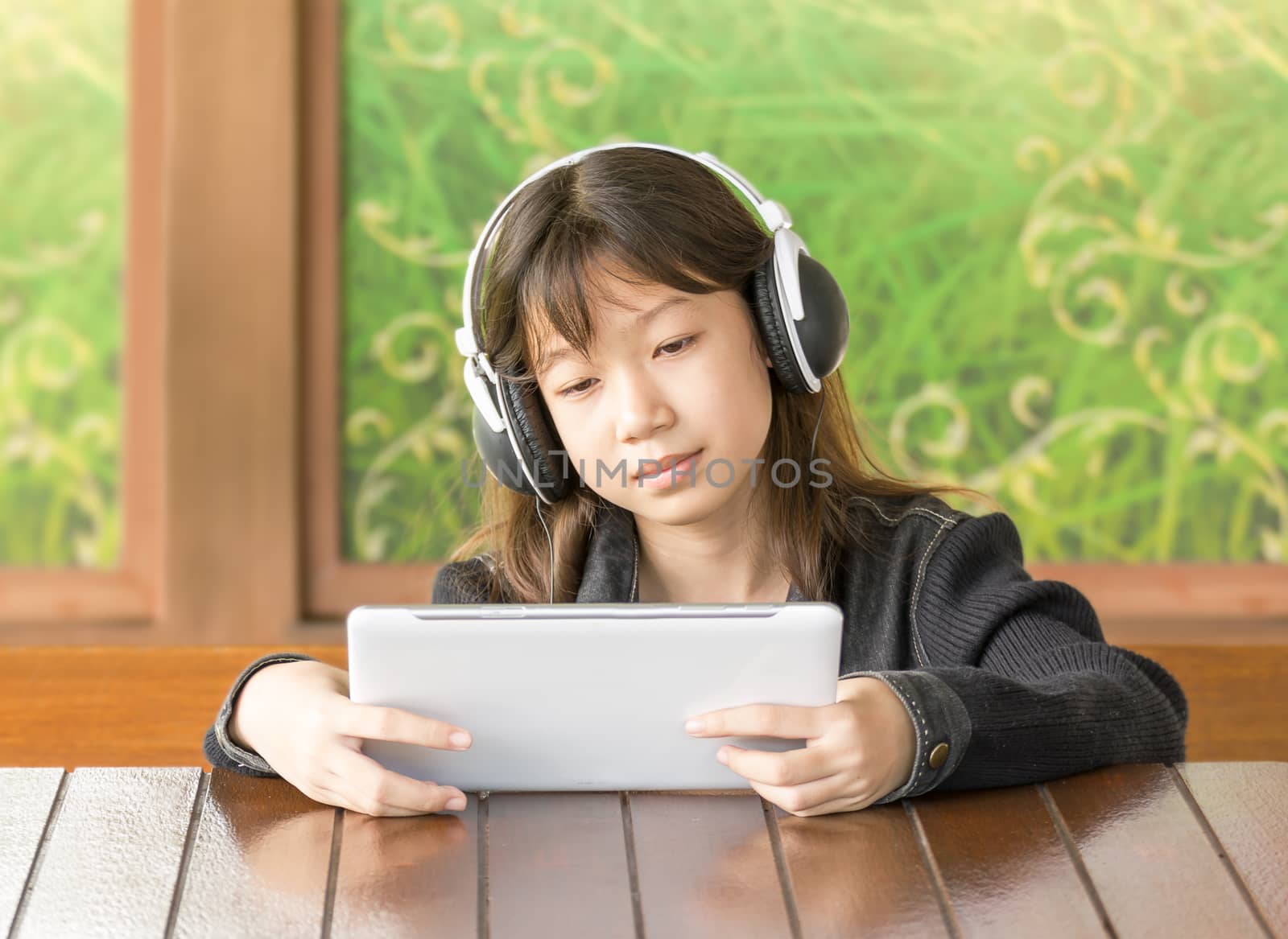 Portrait asian young girl is listening to music through headphones by sitting using Digital Tablet