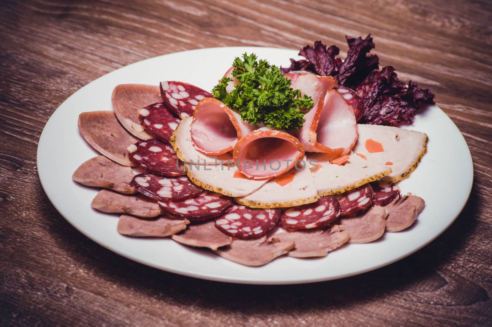 cut meat platter on white plate with greens