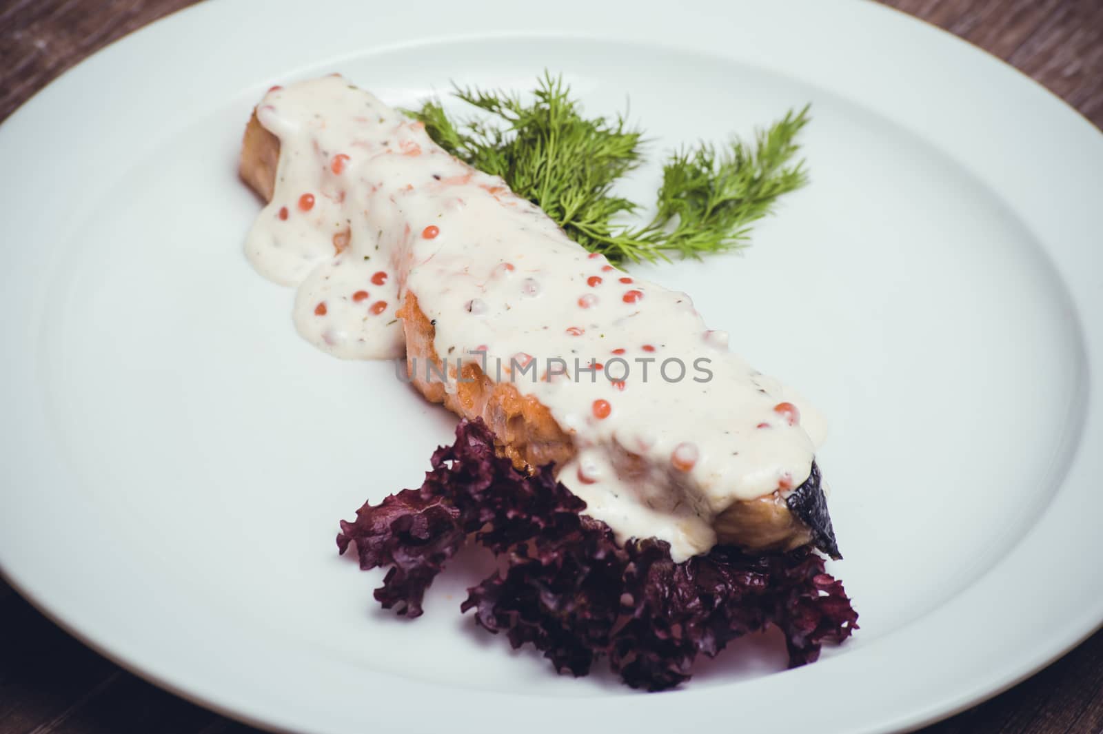 salmon fillet with caviar cream sauce on white plate 